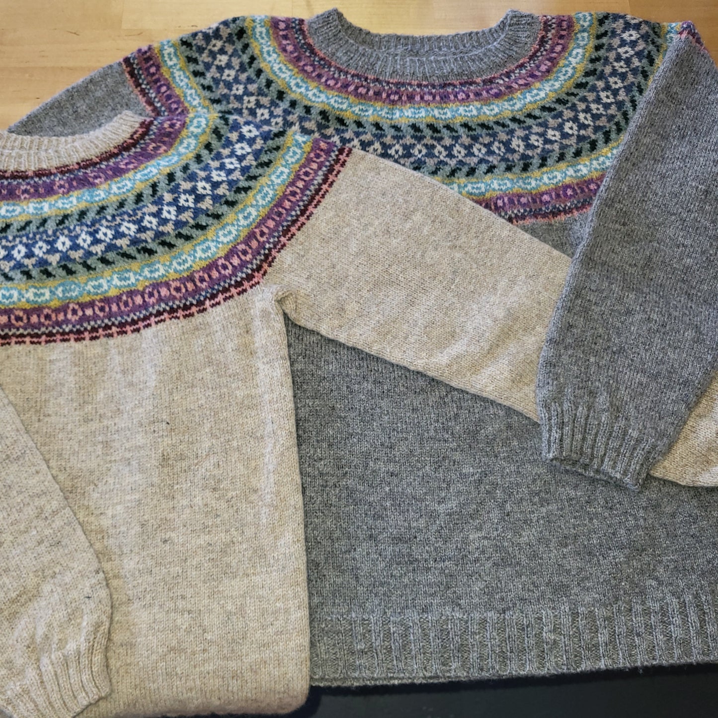 Close-up of a gray and beige fair isle sweater with patterned sleeve on a wooden surface